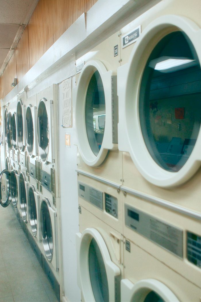 services-01 Interior view of a clean and organized laundromat with multiple washing machines lined up.