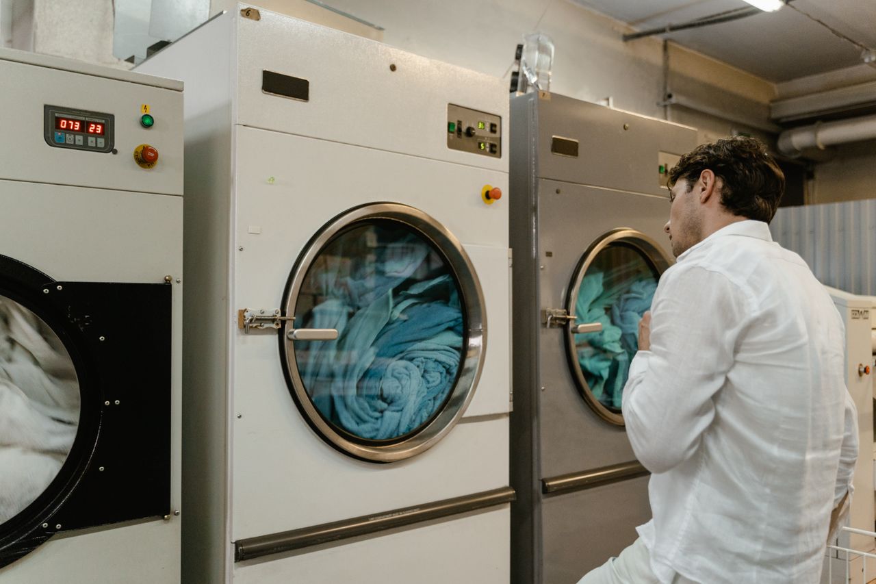 services-02 A man wearing a white shirt uses industrial washing machines in a public launderette.