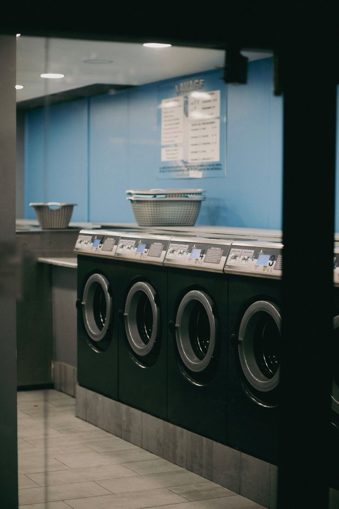 services-02 Interior view of a modern laundromat with multiple washing machines lined up.